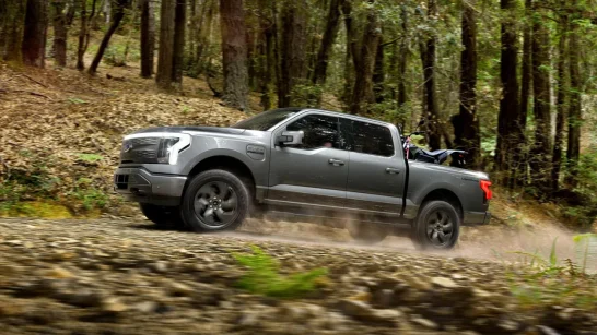 Gray pickup truck driving fast on a dirt road through a forest, kicking up dust in the woods.