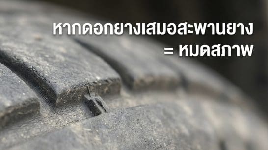 Close-up of a dusty car tire tread with Thai warning text about worn tires indicating they’re unsafe or out of condition