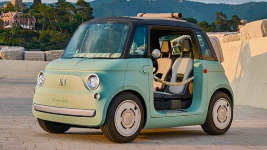 Mint green vintage Fiat 500 with the driver's door open, parked on a stone plaza with hills in the background.