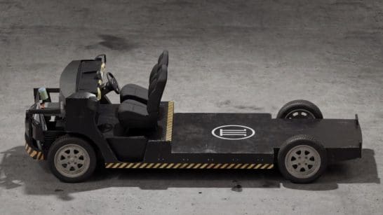 Industrial tow tractor with open cockpit and single seat on a flatbed platform, parked on a concrete floor with yellow-black safety stripes along the base.