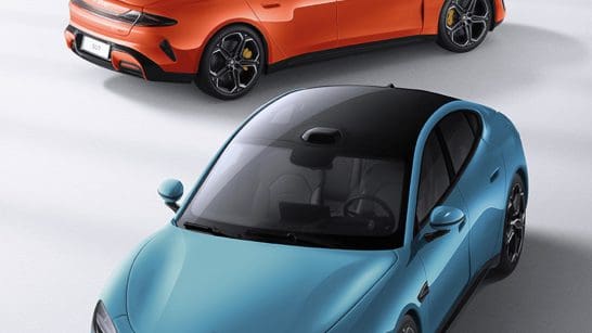 Two sports cars seen from above: a blue sedan in front and an orange SUV behind, on a light surface.